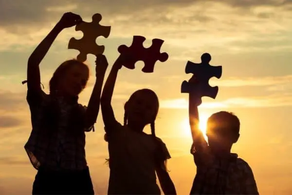 Three Kids Raising Pieces Of Jigsaw Puzzle In Sunset