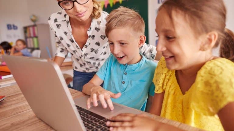 A Girl And A Boy Sitting At A Laptop With Their Mom